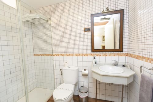 Baño del Hostal Atalaya en Minas de Ríotinto con azulejos blancos, lavabo, inodoro y espejo