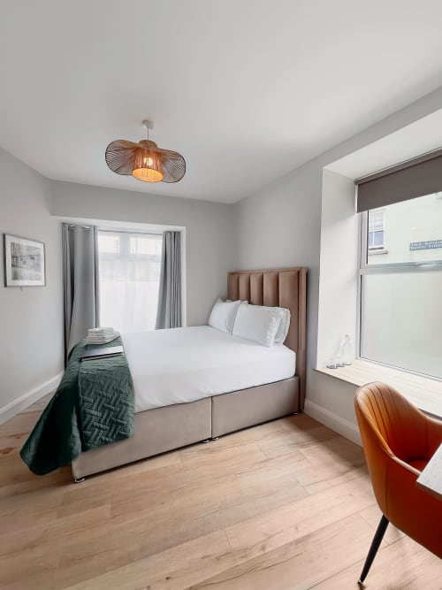Modern double bedroom at Madeline's Accommodation in Wicklow with tan headboard, white bedding, wooden floor, and mountain