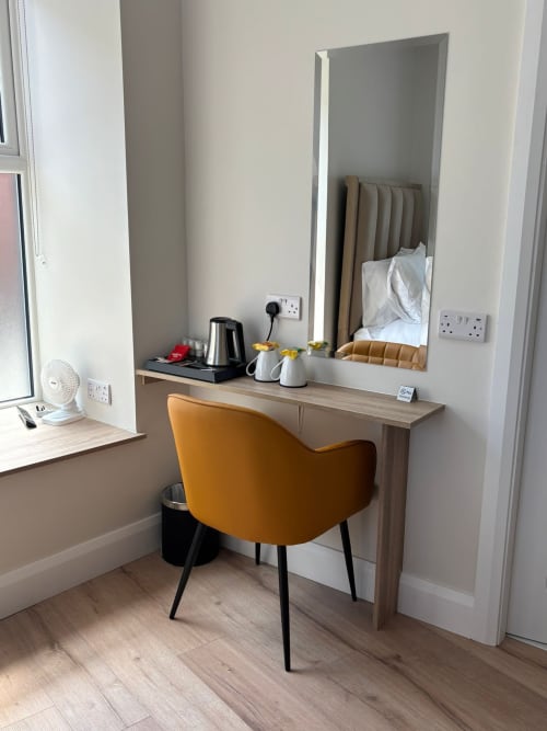 Modern hotel room desk with orange chair, mirror, kettle, and white bedding at Madeline's Accommodation in Wicklow