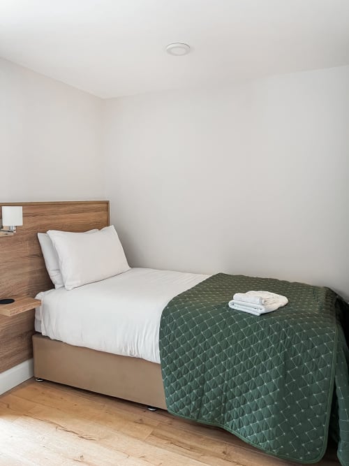 Twin room at Madeline's Accommodation in Wicklow with single bed, white pillows, green quilted throw, and wooden headboard
