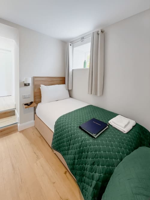 Twin bedroom at Madeline's Accommodation in Wicklow with wooden bed frame, green quilt, white pillows, and large window with