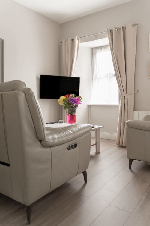 Modern King Studio at Madeline's Accommodation in Wicklow with cream leather recliner, flat-screen TV, colorful flowers, and
