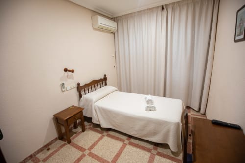 Acogedora habitación individual en el hotel San Poul de Consuegra con cama de madera, ropa de cama blanca, aire acondicionado y vistas a la ciudad