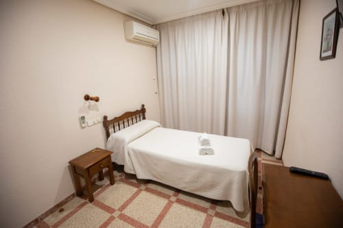 Habitación individual en el hotel San Poul de Consuegra con cama de madera, sábanas blancas, aire acondicionado y vistas a la ciudad