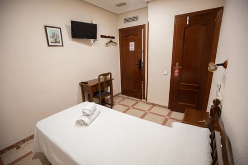 Habitación individual del hotel San Poul en Consuegra con cama blanca, muebles de madera, TV mural y puertas marrones