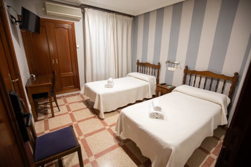 Habitación doble del hotel San Poul en Consuegra con dos camas individuales, muebles de madera y paredes a rayas