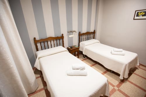 Habitación doble del Hotel San Poul en Consuegra con dos camas de madera, paredes a rayas y vistas a la ciudad