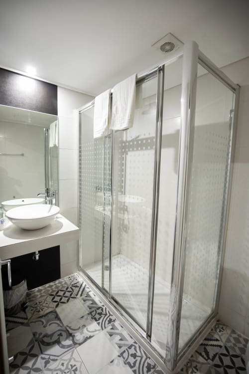 Baño moderno del hotel San Poul en Consuegra con ducha de cristal, lavabo de cerámica blanca y baldosas decorativas