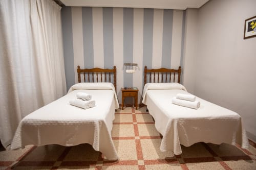 Habitación doble en hotel San Poul de Consuegra con dos camas individuales, paredes a rayas y piso de baldosas
