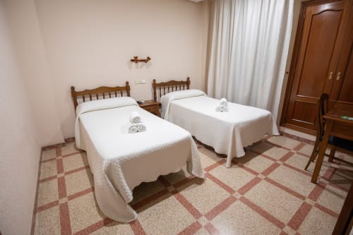 Habitación doble en el hotel San Poul de Consuegra con dos camas individuales, marcos de madera, ropa blanca y suelo de baldosas