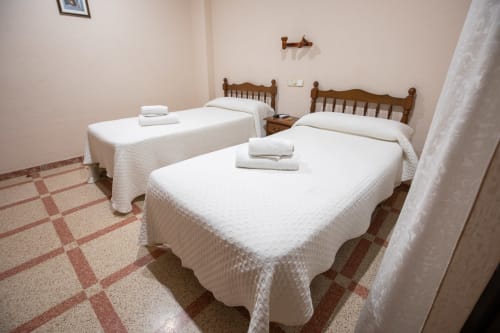 Habitación doble en el hotel San Poul de Consuegra con dos camas individuales, sábanas blancas, cabeceros de madera y suelo de baldosas