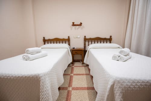 Dos camas individuales con sábanas blancas y toallas enrolladas en una habitación doble del hotel San Poul en Consuegra