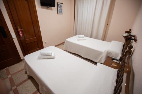 Habitación doble con dos camas individuales en el hotel San Poul de Consuegra, con ropa de cama blanca y muebles de madera
