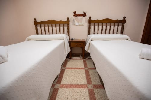 Dormitorio doble en el hotel San Poul de Consuegra con dos camas individuales, cabeceros de madera y suelo de baldosas de barro