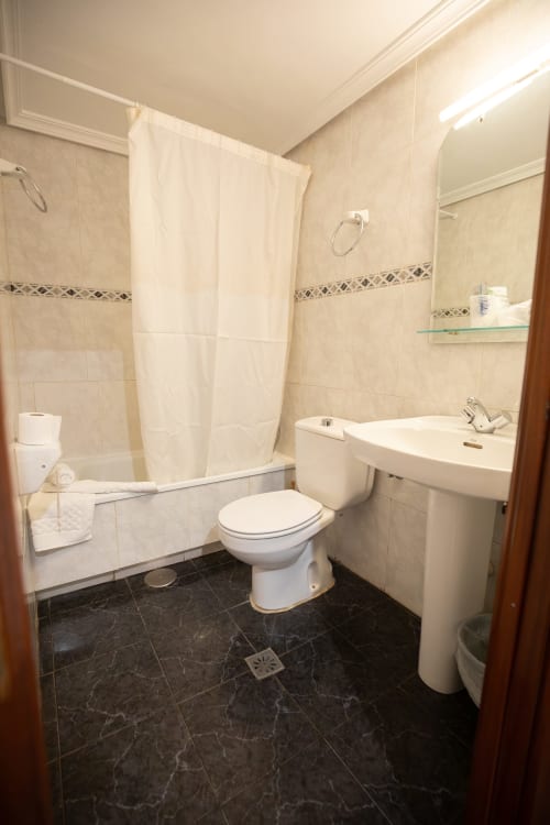Moderno baño del hotel San Poul en Consuegra con ducha, lavabo blanco, inodoro y piso de azulejos oscuros