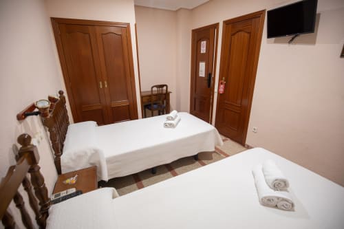 Habitación doble con dos camas individuales en el hotel San Poul de Consuegra, España, con puertas de madera y televisor
