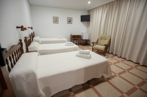 Habitación triple del hotel San Poul en Consuegra con tres camas, muebles de madera, televisor y ventanas con cortinas