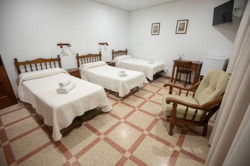 Habitación triple del hotel San Poul en Consuegra con tres camas de madera, sábanas blancas y mobiliario tradicional