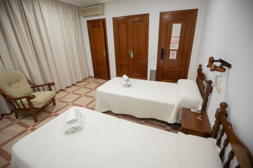 Habitación triple del hotel San Poul en Consuegra con dos camas, muebles de madera y decoración tradicional