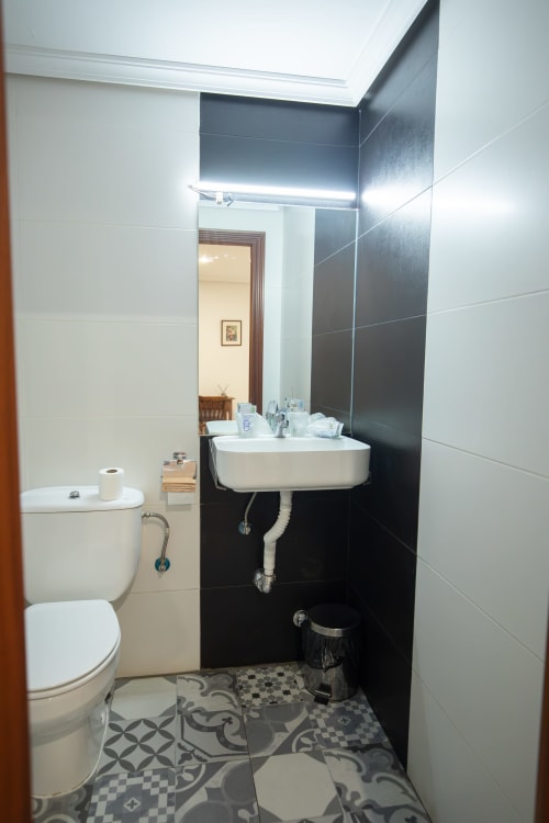 Baño moderno del hotel San Poul en Consuegra con azulejos blanco y negro, lavamanos mural e iluminación LED