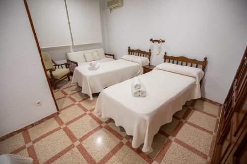 Habitación cuádruple del hotel San Poul en Consuegra con tres camas, muebles de madera y piso de baldosas