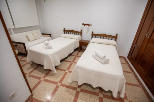 Habitación cuádruple del hotel San Poul en Consuegra con dos camas de madera, ropa de cama blanca y piso de baldosa de terracota
