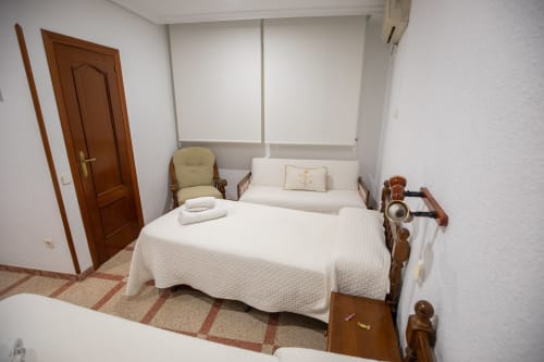 Acogedora habitación cuádruple del hotel San Poul en Consuegra con ropa de cama blanca, puerta de madera, sillón y piso de baldosas