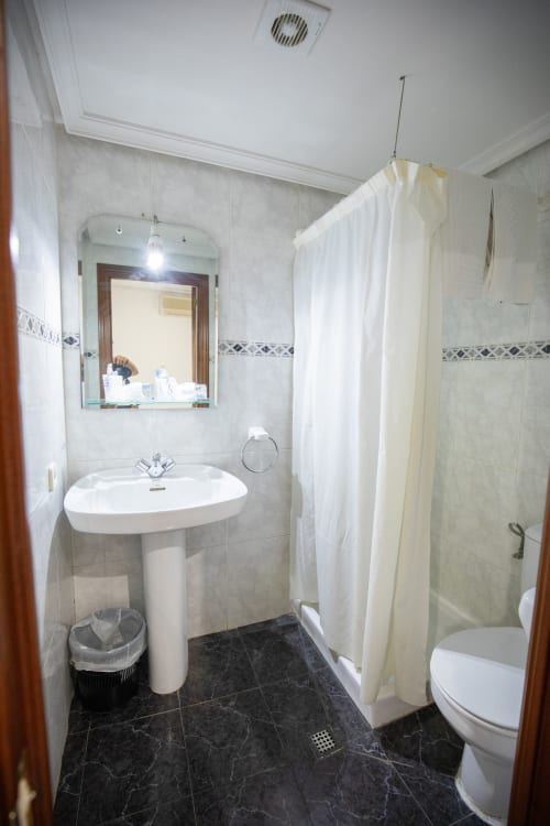 Baño moderno del hotel San Poul en Consuegra con lavabo de pedestal, ducha y piso de azulejos oscuros