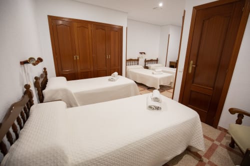 Habitación cuádruple del hotel San Poul en Consuegra con tres camas, armario de madera, puertas marrones y suelo de baldosas.