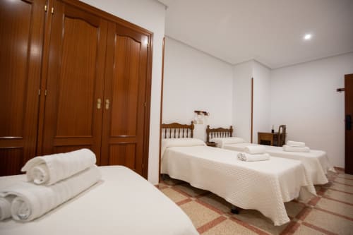 Amplia habitación cuádruple en el hotel San Poul de Consuegra con cuatro camas, armario de madera y sábanas blancas