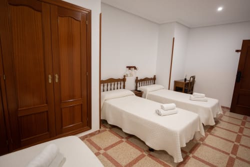 Amplia habitación cuádruple en el hotel San Poul de Consuegra con tres camas individuales, muebles de madera y piso de baldosas.