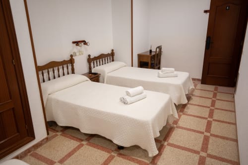 Habitación triple del hotel San Poul en Consuegra con tres camas individuales, muebles de madera y piso de baldosa de barro