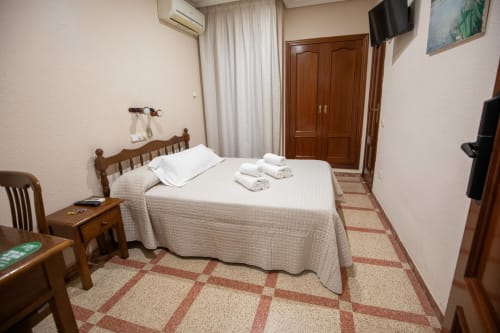 Habitación doble en Hotel San Poul de Consuegra con cama de madera, ropa blanca, TV y decoración tradicional
