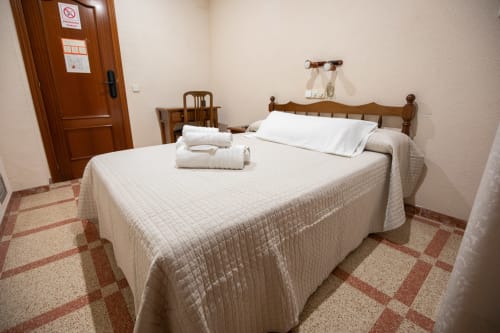 Habitación doble del hotel San Poul en Consuegra con cama de madera, sábanas blancas y piso de baldosa terracota