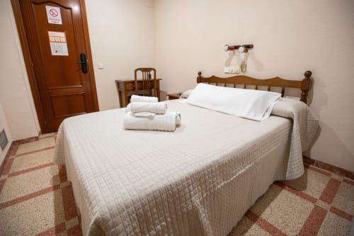 Habitación doble del hotel San Poul en Consuegra con cama de madera, sábanas blancas y piso de baldosa terracota