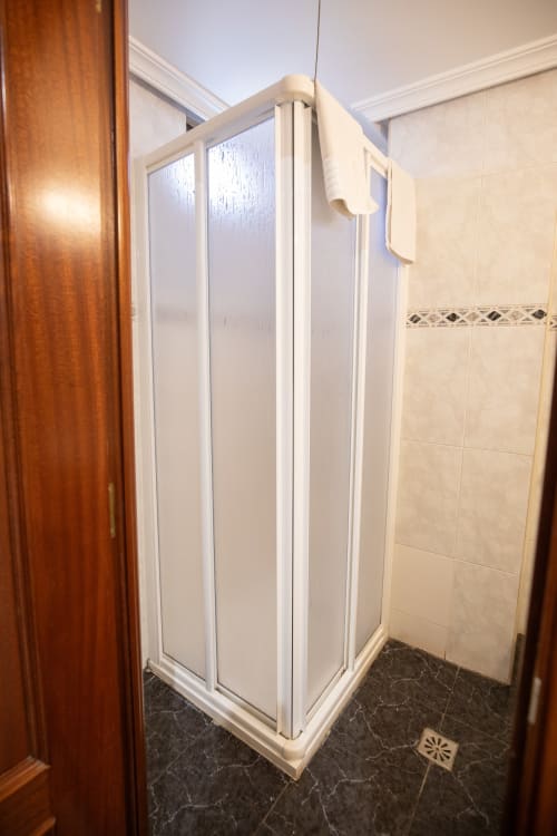 Moderno plato de ducha con marco blanco y puertas de vidrio texturizado en el baño del hotel San Poul, Consuegra