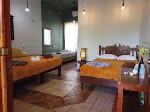 Habitación tradicional en el hostel Cayuco Maya de Bacalar con camas de madera, ropa de cama naranja y lámparas colgantes modernas
