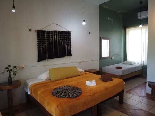 Luminoso dormitorio tradicional en el hostal Cayuco Maya de Bacalar con cama naranja, macramé negro en la pared y detalles verde