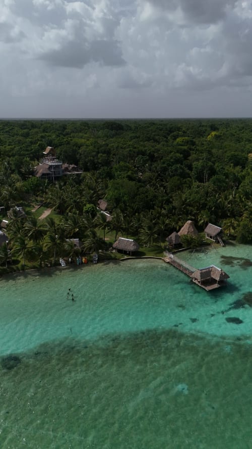 Vista aérea del hostal Cayuco Maya en Bacalar con bungalós de techo de palapa, laguna turquesa y exuberante dosel de selva