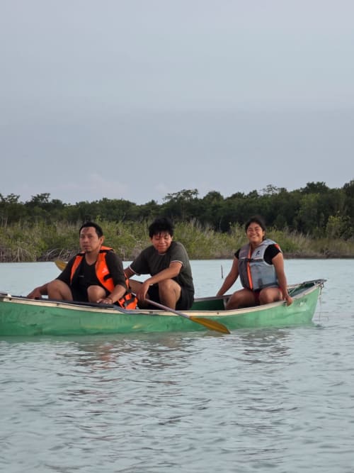 Tres personas en un kayak verde sobre aguas turquesas en el hostal Cayuco Maya de Bacalar, México, con manglares al fondo