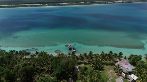 Vista aérea del hostal Cayuco Maya en Bacalar con cabañas tradicionales frente a las aguas turquesas del lago y palmeras