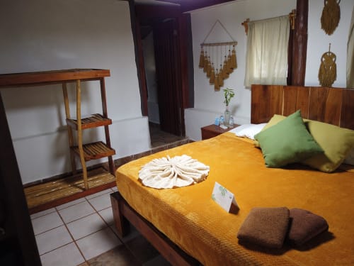 Dormitorio de Cabaña Tradicional en el hostel Cayuco Maya de Bacalar con cama de madera, ropa de cama amarilla y almohadas verdes