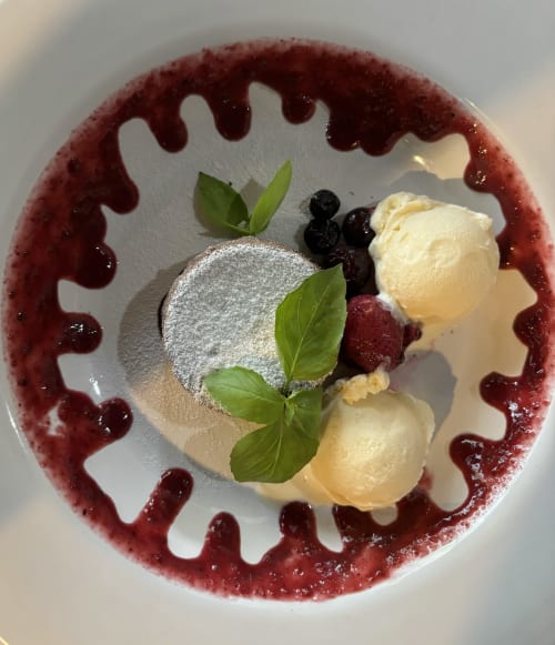 Elegante plato de postre en el hostel Cayuco Maya de Bacalar con torta espolvoreada, helado de vainilla, frutos rojos y decoración de menta