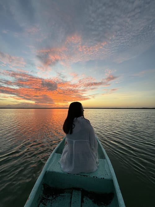 Mujer en camisa blanca en una cayuca al atardecer, vista del lago Bacalar desde el hostal Cayuco Maya