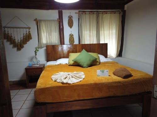 Habitación del hostal Cayuco Maya en Bacalar con cama de madera, ropa de cama amarilla, almohada verde y decoración boho