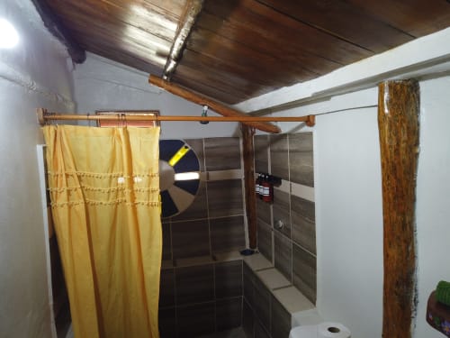 Baño rústico en la Cabaña Tradicional del hostal Cayuco Maya, Bacalar, con vigas de madera y cortina de ducha amarilla