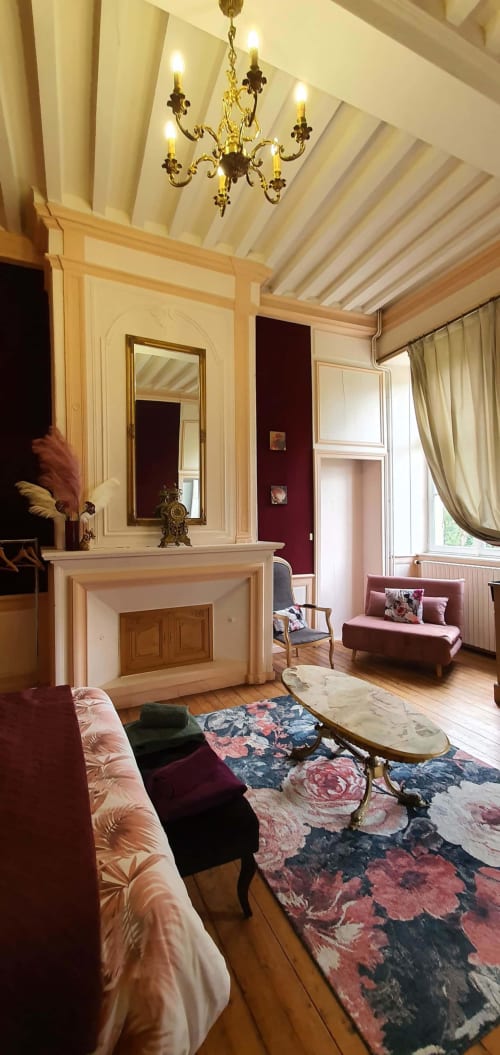 Élégant salon du Manoir de Saint-Ouen avec cheminée, mobilier bordeaux, lustre ouvragé et tapis floral