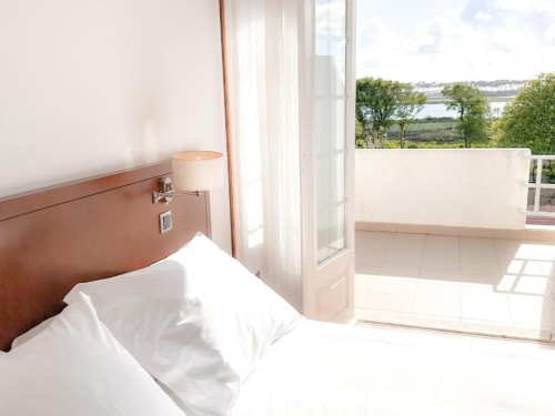 Bright hotel room at Hotel Slow Stay in Esposende with bed, lamp, and balcony overlooking river and countryside