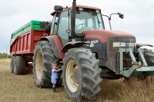 Jeune enfant debout près d'un tracteur rouge New Holland avec remorque dans les terres agricoles rurales près de Saint-Hilaire-sur-Puiseaux