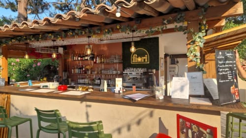 Bar Fiori de l'hôtel ALMA ROSSA à Lecci, avec comptoir en bois, sièges verts et vue sur le jardin